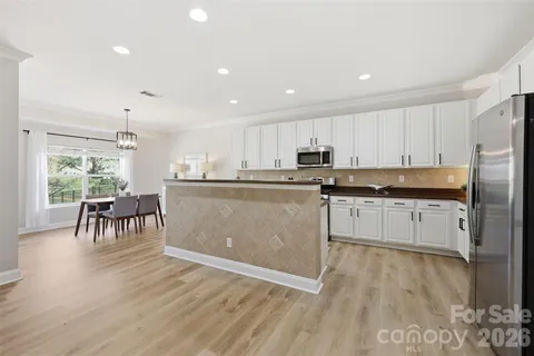 a kitchen with stainless steel appliances granite countertop a stove a sink a refrigerator and white cabinets with wooden floor