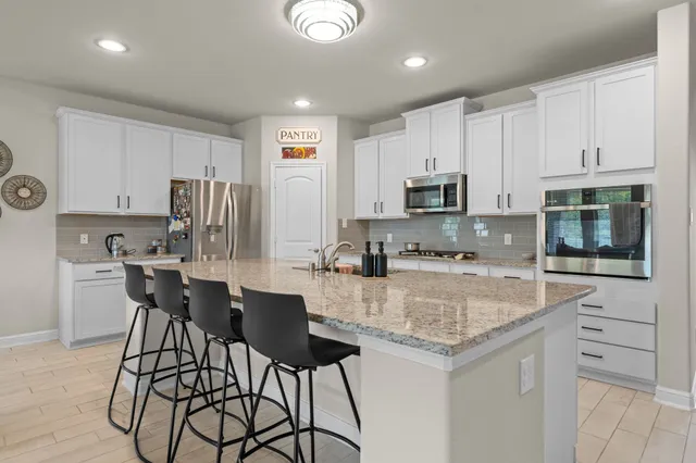 a kitchen with stainless steel appliances granite countertop a stove top oven a refrigerator a sink and white cabinets with wooden floors