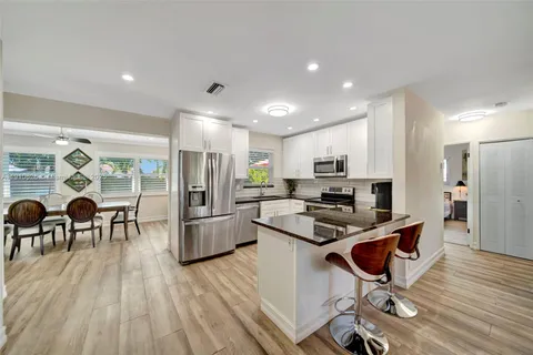 a kitchen with stainless steel appliances kitchen island granite countertop a refrigerator oven a stove a dining table and chairs with wooden floor