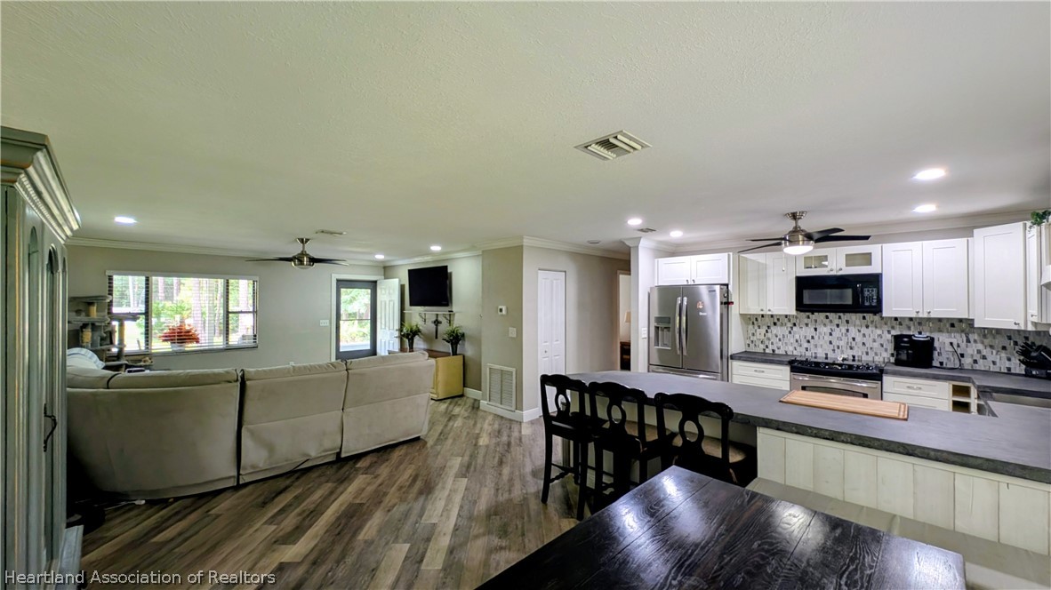 6218 Apple Road Sebring, FL 33875 - Photo 11 of 40 a large living room with stainless steel appliances kitchen island granite countertop a table chairs in it and a flat screen tv