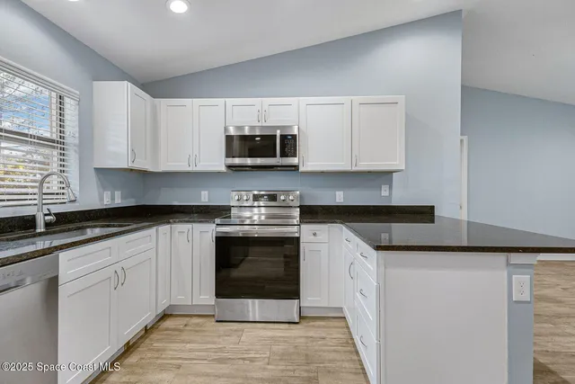 a kitchen with stainless steel appliances granite countertop a refrigerator a sink and white cabinets