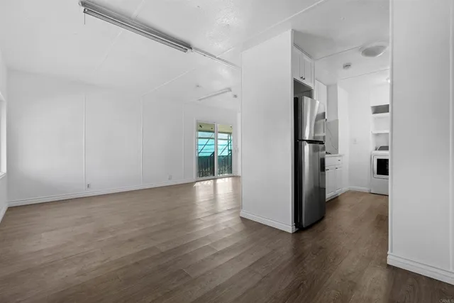 a view of a refrigerator in kitchen and an empty room with wooden floor