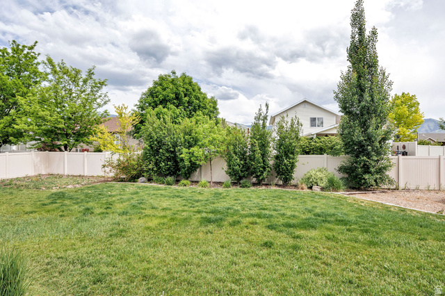 2912 South 1080th Street West Logan, UT 84321 - Photo 43 of 43 Expansive green lawn surrounded by mature trees and shrubs, featuring a light-toned privacy fence