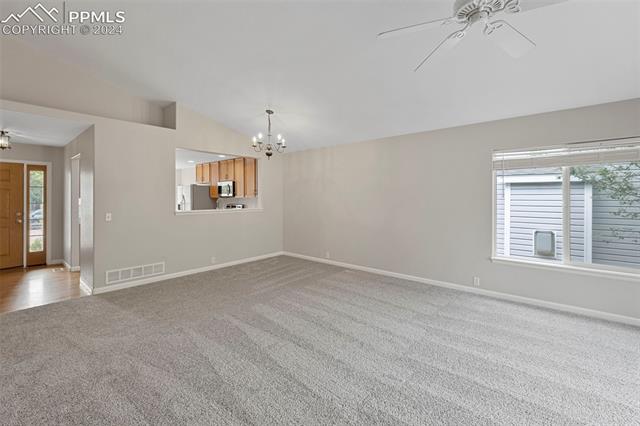 6725 Akron Road Colorado Springs, CO 80923 - Photo 13 of 50 Unfurnished living room featuring carpet flooring, lofted ceiling, and ceiling fan with notable chandelier