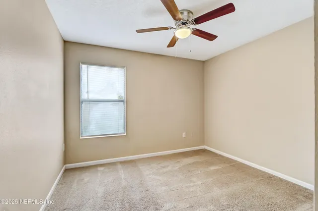 an empty room with a chandelier fan and windows