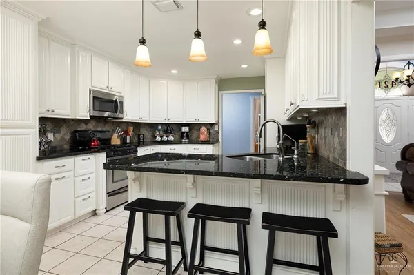 a kitchen with stainless steel appliances granite countertop a stove top oven a refrigerator a sink and white cabinets