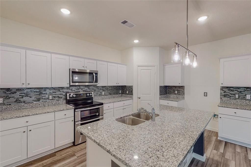 407 Madison Way Princeton, TX 75407 - Photo 34 of 40 Kitchen featuring stainless steel appliances, backsplash, light wood-type flooring, white cabinetry, and an island with sink