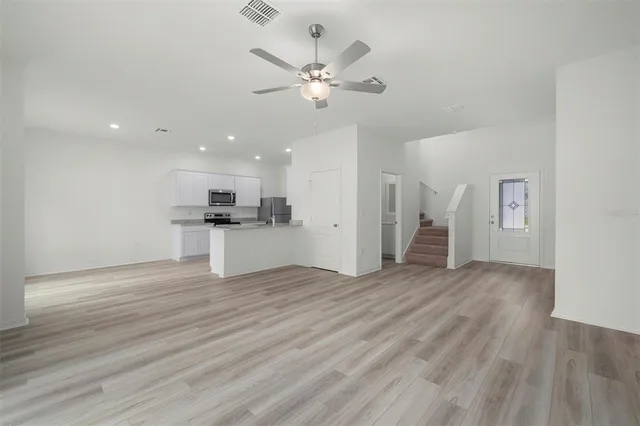 a view of an empty room with wooden floor and a ceiling fan