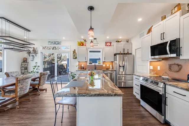 a kitchen with stainless steel appliances granite countertop a stove top oven a sink dishwasher and white cabinets with wooden floor