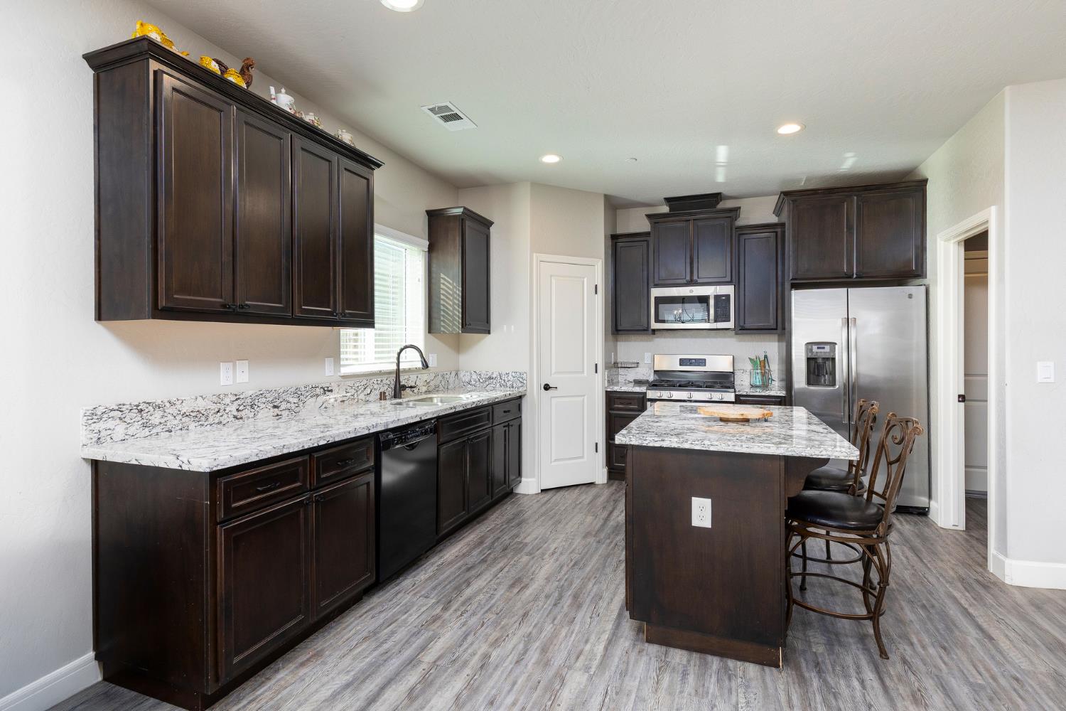 1374 South Enns Avenue Reedley, CA 93654 - Photo 14 of 48 a kitchen with kitchen island granite countertop wooden floors stainless steel appliances a sink and a refrigerator
