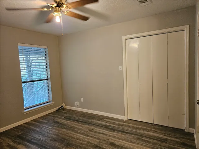 an empty room with wooden floor fan and windows