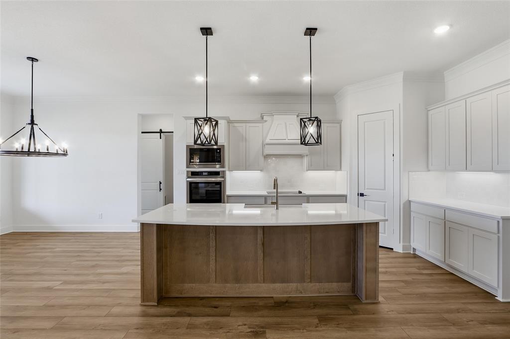 810 Vly Rdg Road Van Alstyne, TX 75495 - Photo 11 of 39 Dual tone kitchen featuring a barn door, two tone cabinets, decorative light fixtures, an island with sink, and decorative backsplash