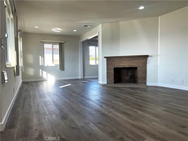 an empty room with wooden floor fireplace and windows