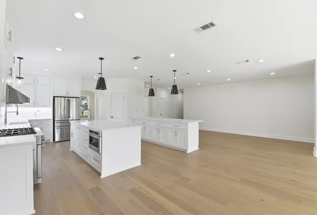 a large white kitchen with kitchen island a stove a sink a refrigerator and white cabinets with wooden floor