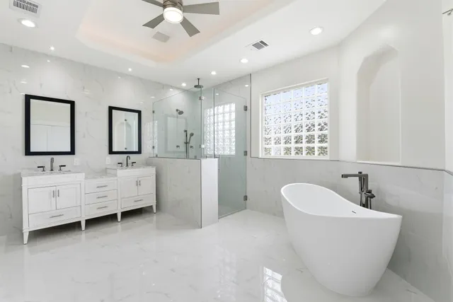 a bathroom with a double vanity sink a mirror a bathtub and a window