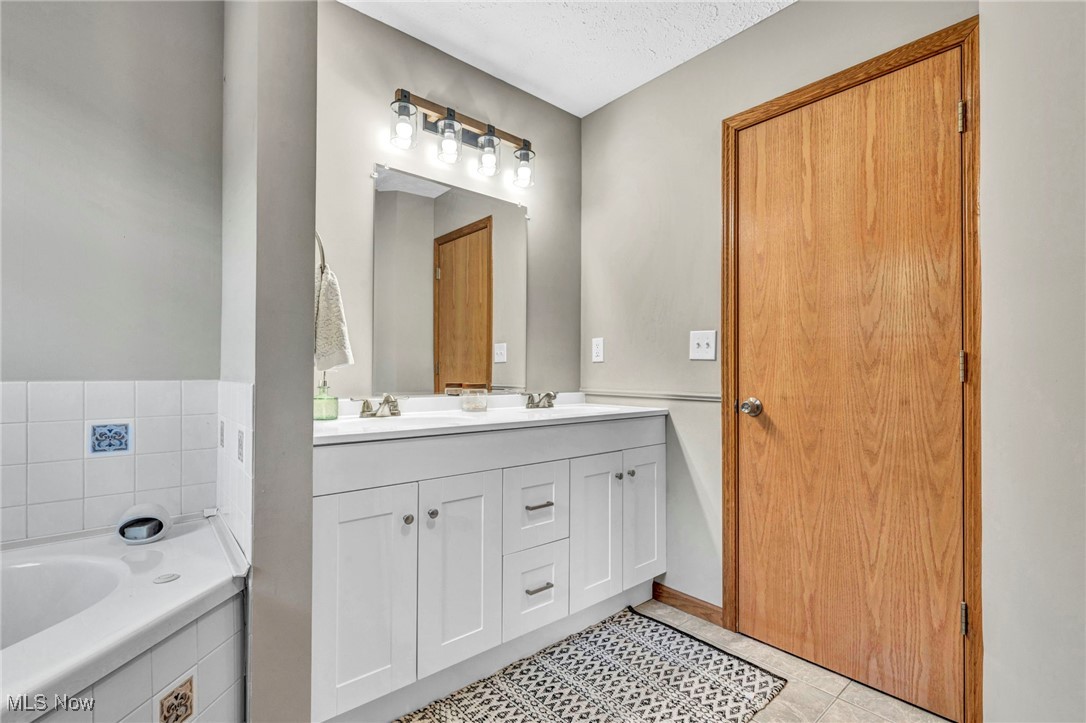 14902 Kneisel Road Vermilion, OH 44089 - Photo 24 of 49 Bathroom featuring tile patterned flooring, tiled tub, vanity, and a textured ceiling