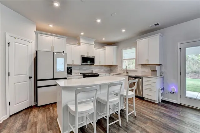 a kitchen with stainless steel appliances a stove top oven a sink refrigerator and a dining table with wooden floor