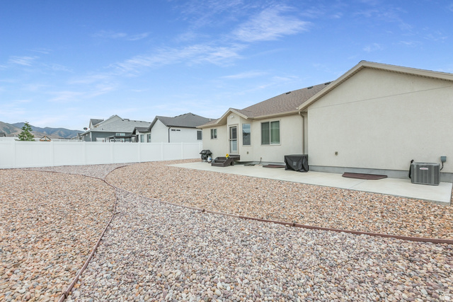 1228 North Providence Way Tooele, UT 84074 - Photo 28 of 28 Spacious gravel backyard featuring a concrete patio, white vinyl fencing, and a neutral stucco exterior