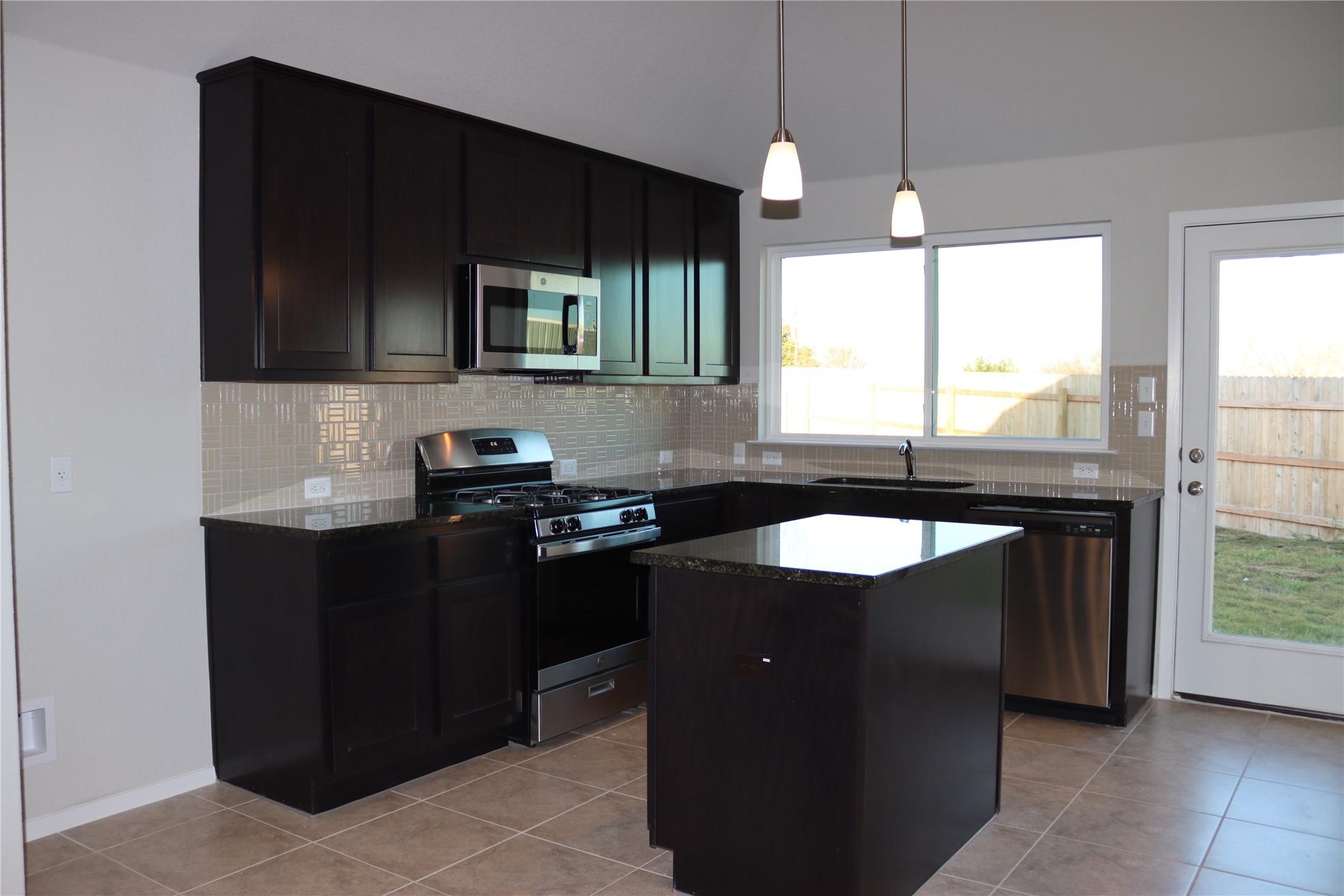 225 Graver Street Georgetown, TX 78626 - Photo 10 of 19 Kitchen with stainless steel appliances, a center island, decorative light fixtures, light tile patterned flooring, and decorative backsplash