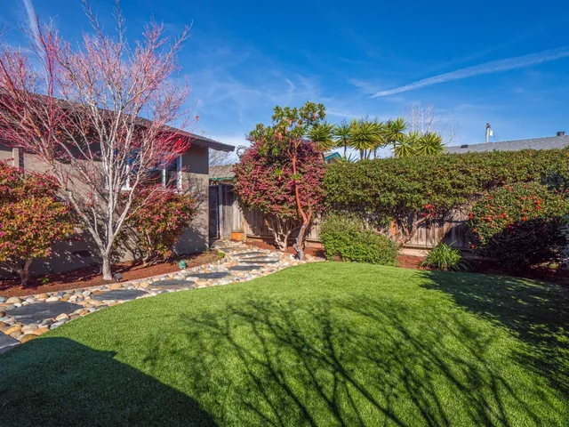 a view of a patio with couches table and chairs under an umbrella with a fire pit and potted plants
