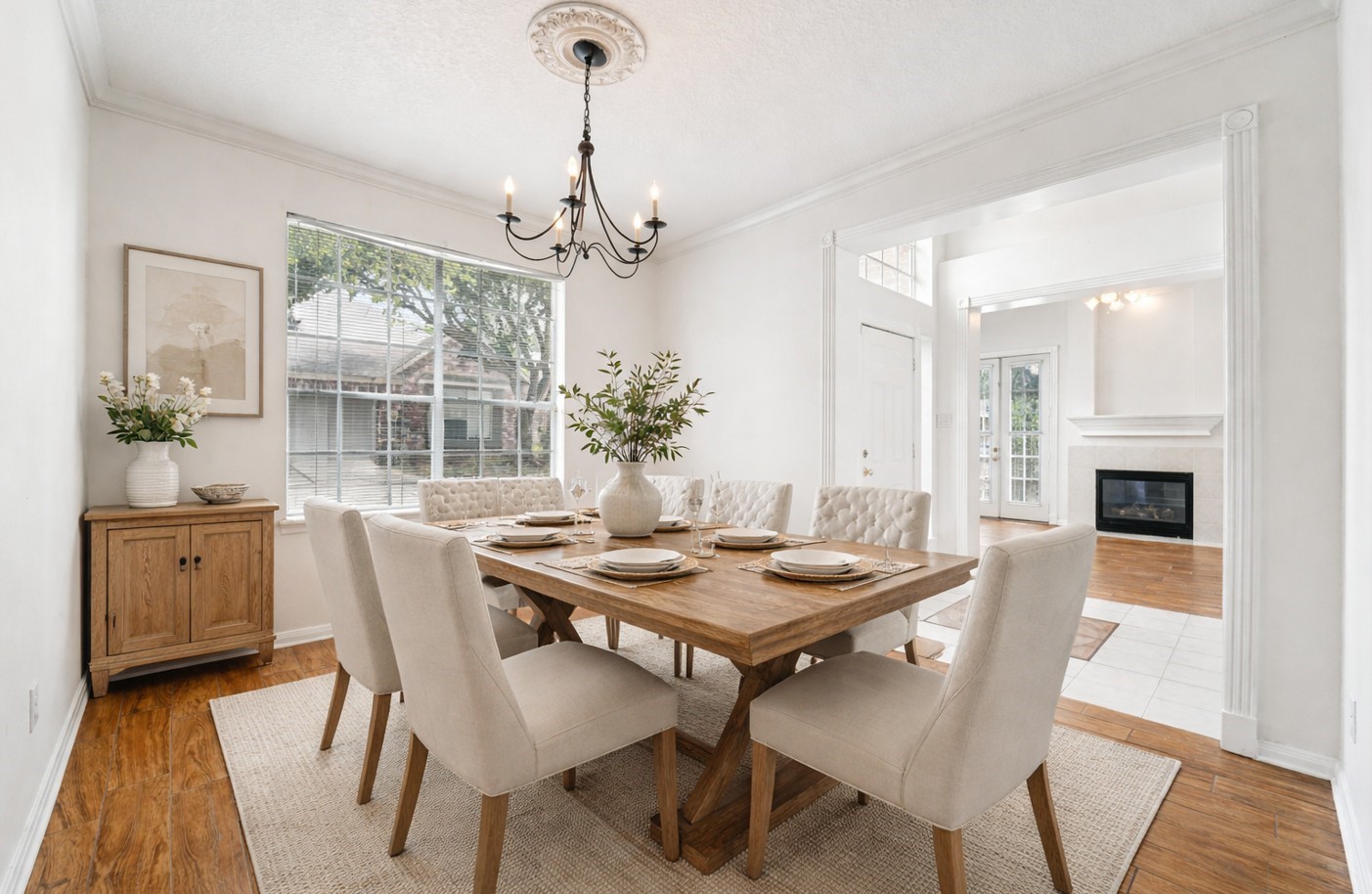 14420 Walters Road, Unit 55 Houston, TX 77014 - Photo 18 of 35 Bright and inviting dining room with a rustic wooden table and elegant upholstered chairs. Features a chic chandelier, large window for natural light, and a view into a cozy living area with a fireplace.