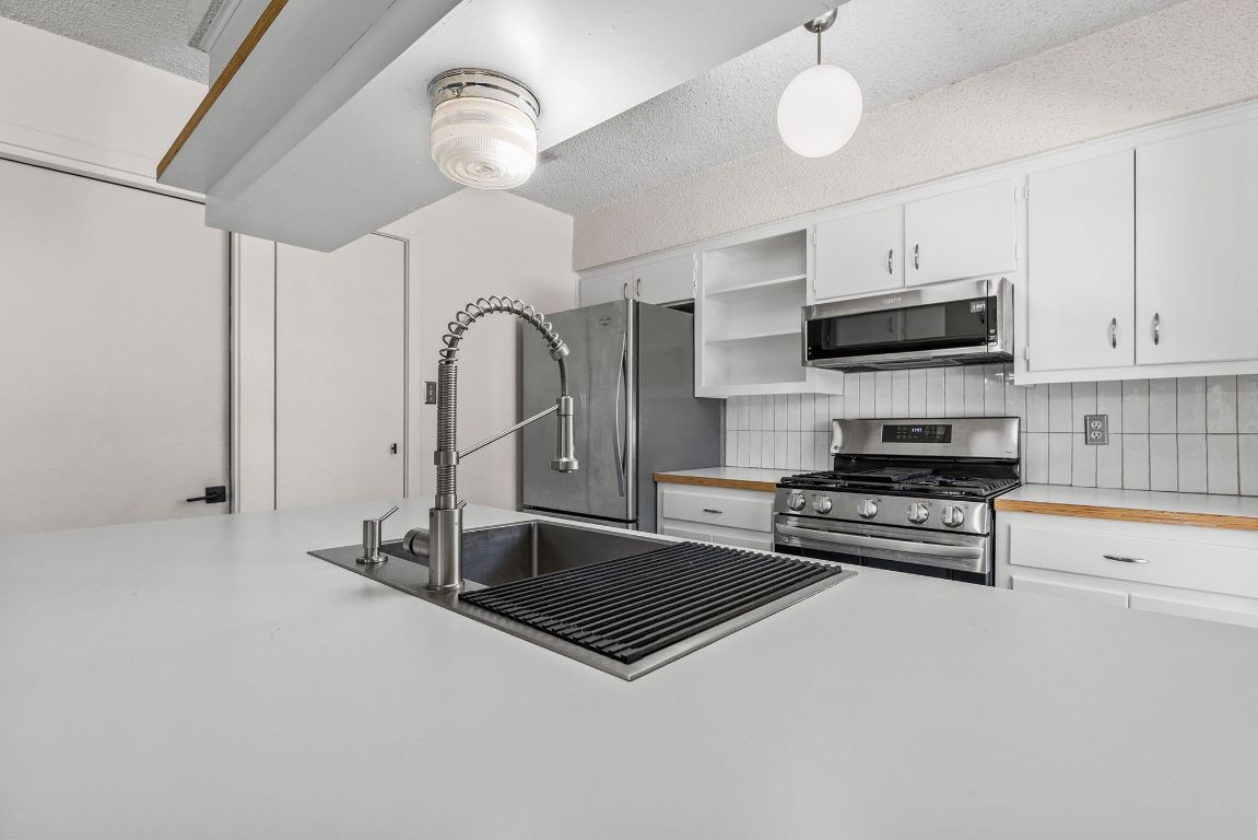 1906 Parkside Lane Austin, TX 78745 - Photo 8 of 40 Kitchen featuring light countertops, stainless steel appliances, white cabinets, and a textured ceiling