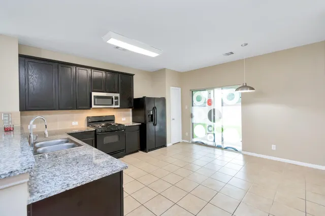 a kitchen with granite countertop a sink a stove top oven a refrigerator cabinets and wooden floor