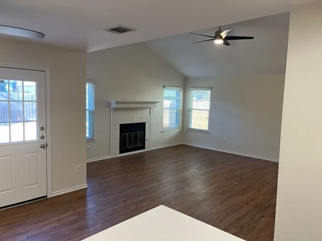 an empty room with wooden floor fireplace and windows