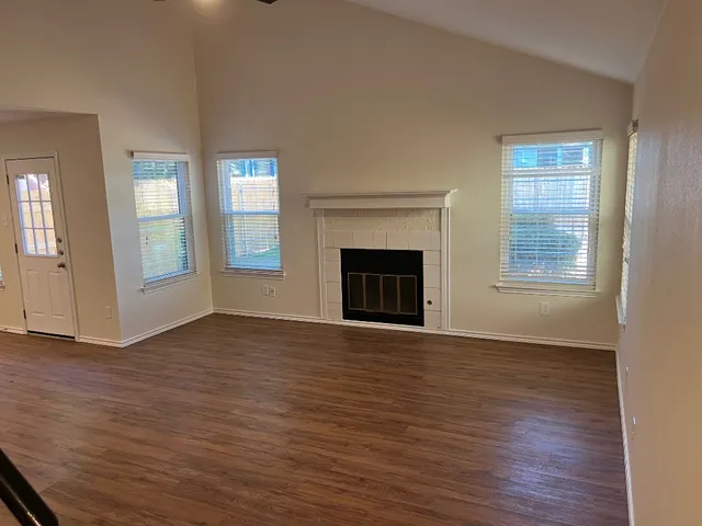 an empty room with wooden floor fireplace and windows