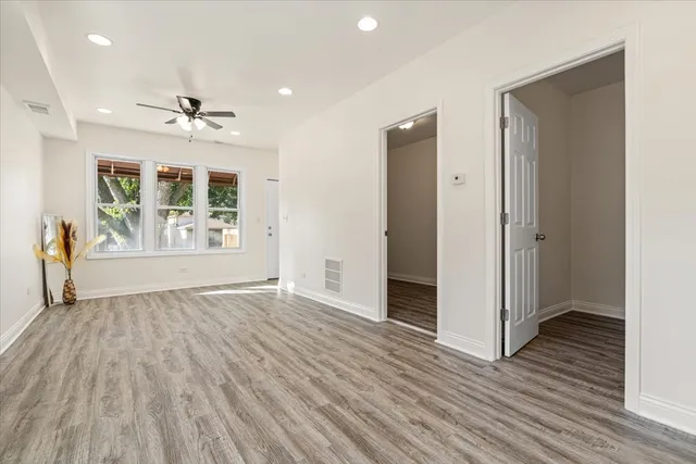 an empty room with wooden floor ceiling fan and windows