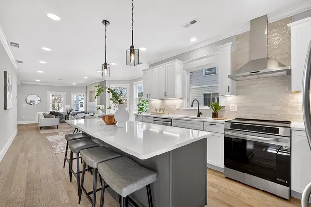 a kitchen with stainless steel appliances granite countertop a stove a refrigerator a kitchen island a sink white cabinets and chairs