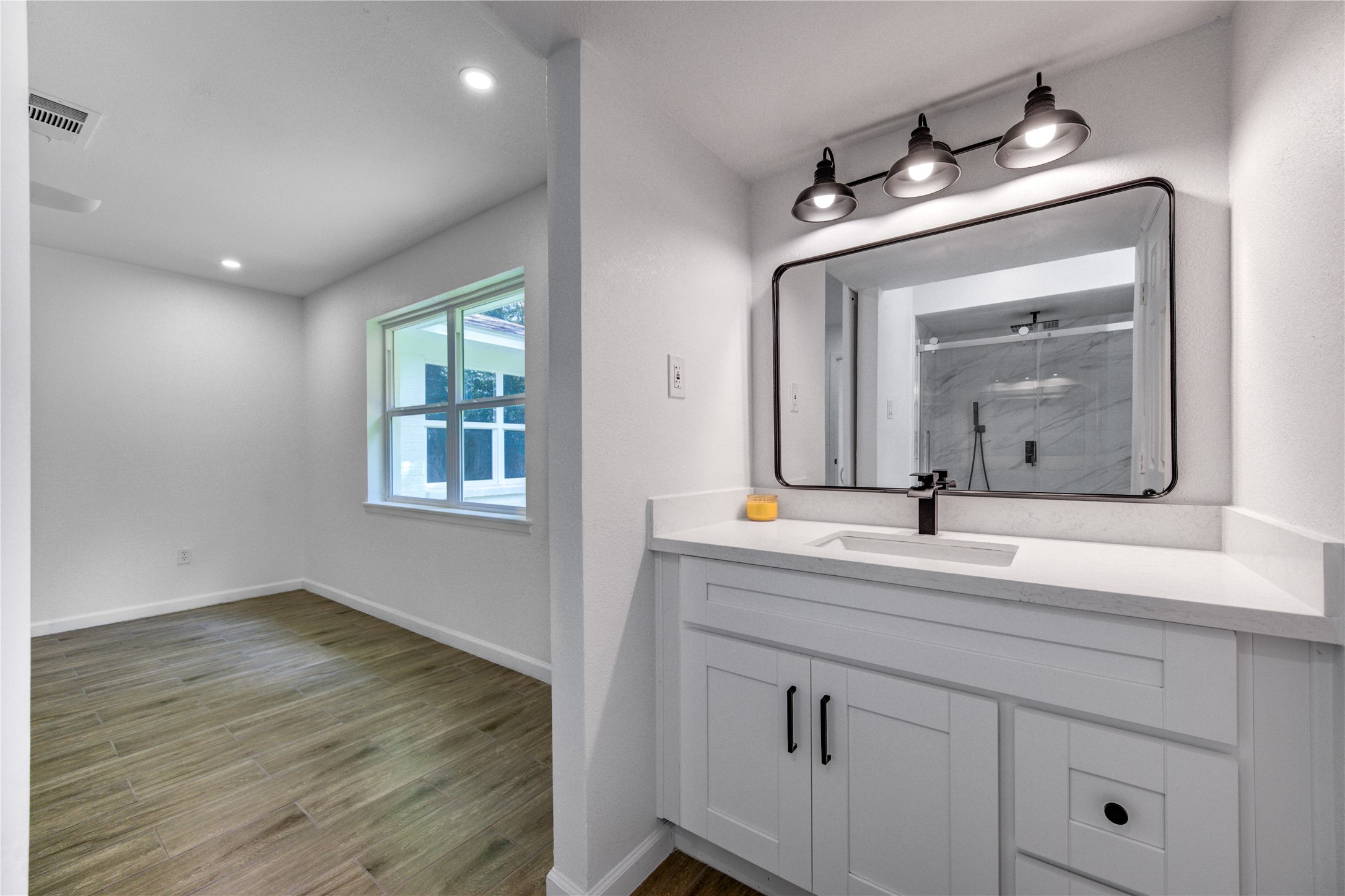 5411 Logston Lane Spring, TX 77389 - Photo 34 of 50 Bright and modern space featuring a sleek bathroom vanity with ample lighting and a view into a cozy, sunlit room with wood-style flooring.