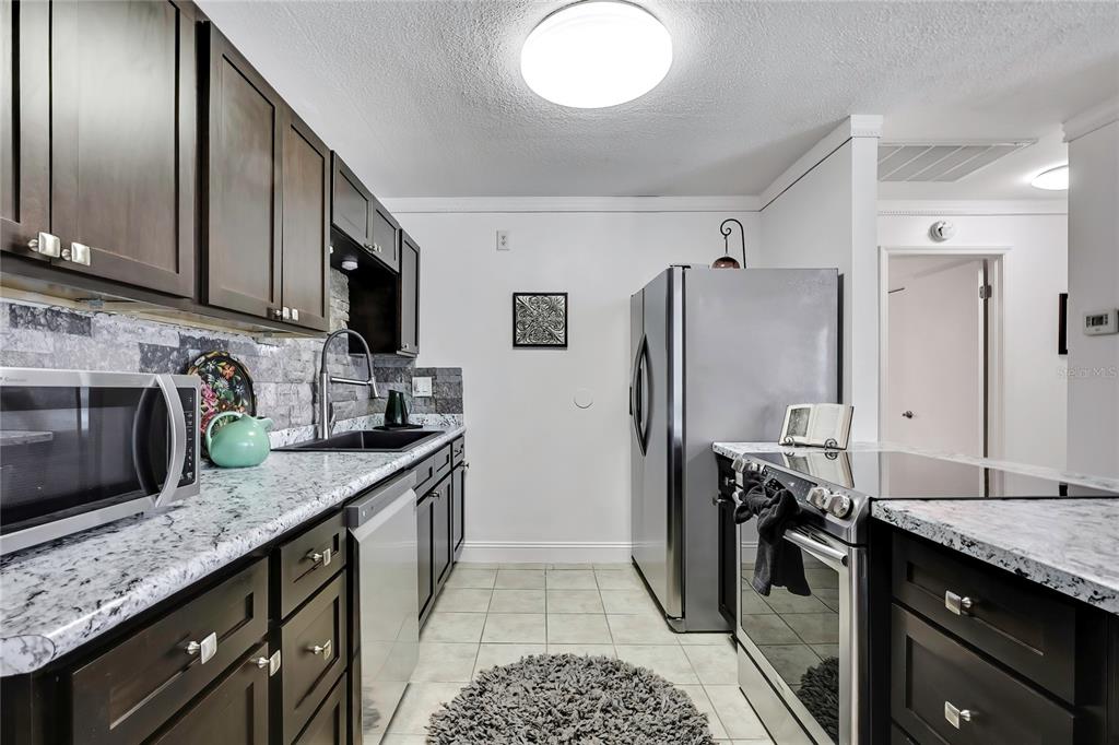 9059 Gaynor Street Spring Hill, FL 34608 - Photo 14 of 36 a kitchen with granite countertop stainless steel appliances a sink stove refrigerator and cabinets