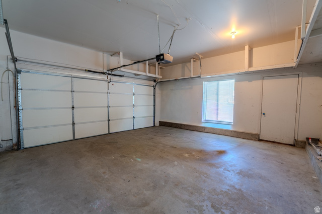 11957 Noelle Road Sandy, UT 84092 - Photo 31 of 38 Spacious garage with a sectional overhead door, concrete flooring, window with blinds, overhead lighting, and built-in shelving