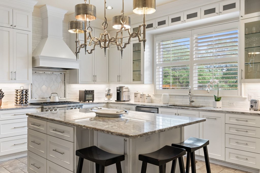 7609 Sandia Loop Austin, TX 78735 - Photo 12 of 40 Gourmet kitchen featuring a central island with bar seating, white shaker cabinetry, stone countertops, a tile backsplash, and plantation-shutter windows