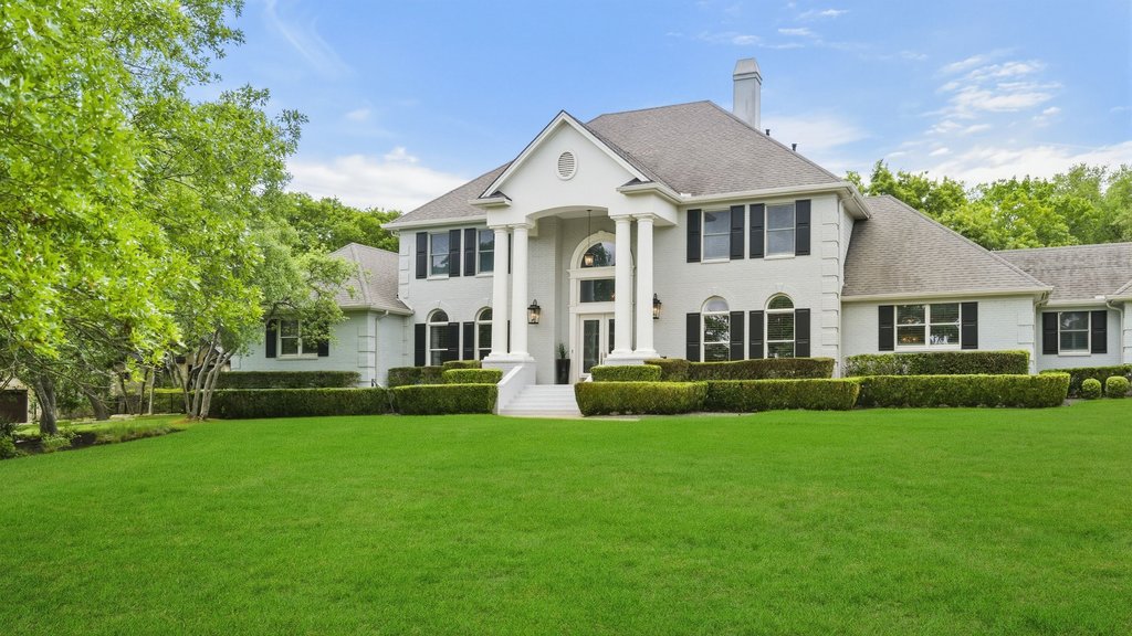 7609 Sandia Loop Austin, TX 78735 - Photo 2 of 40 This stately white brick exterior features grand columns and classic black shutters, creating a commanding presence on a lush, full-acre lot in one of Austin’s premier gated communities.