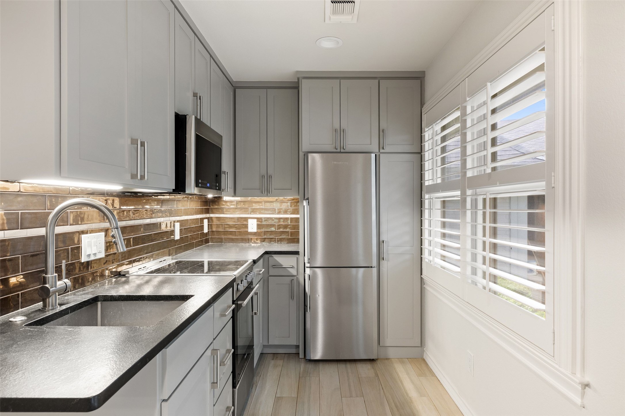 7609 Sandia Loop Austin, TX 78735 - Photo 34 of 40 Modern kitchen featuring light gray cabinetry, stainless steel appliances, dark countertops, and a brick-patterned backsplash