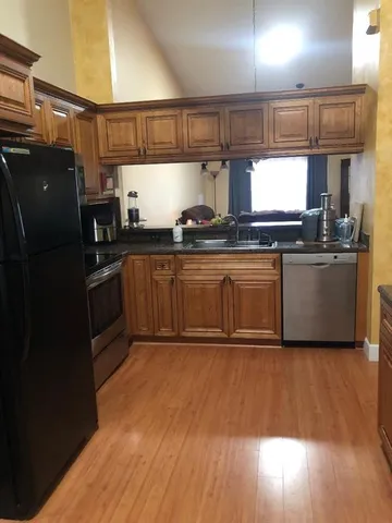 a kitchen with stainless steel appliances granite countertop a sink a stove a refrigerator cabinets and a wooden floor