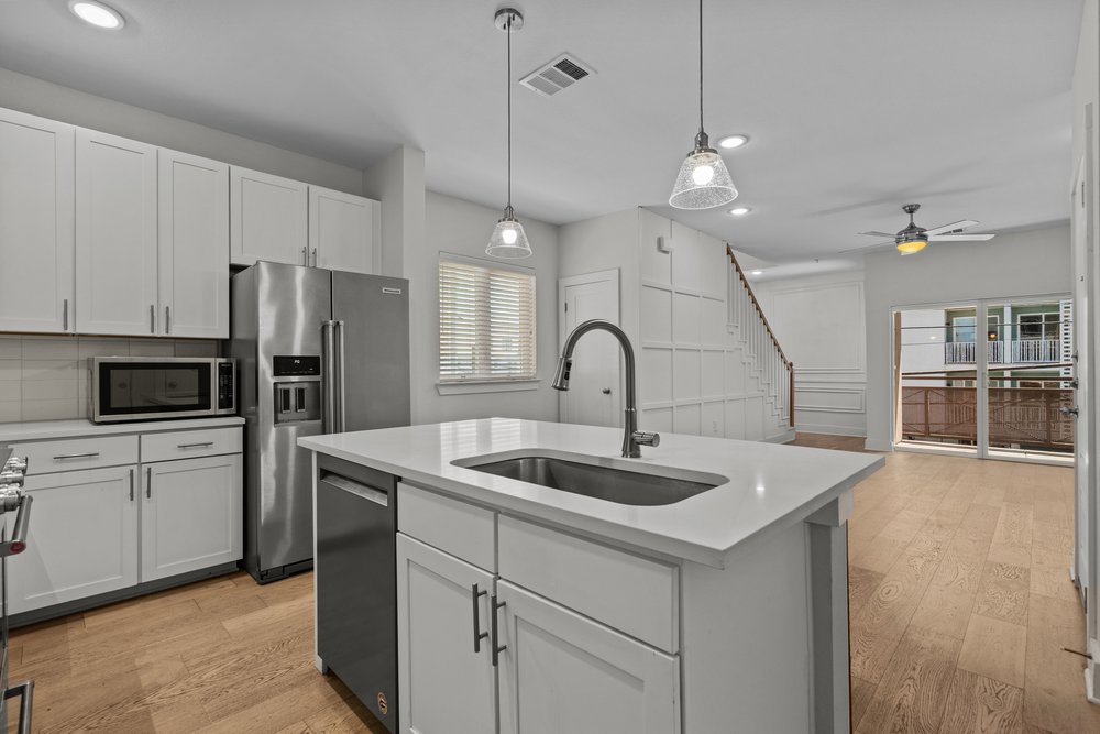 2827 Manor Road, Unit 2201 Austin, TX 78722 - Photo 14 of 40 Kitchen featuring a central island with an undermount sink, pendant lighting, stainless steel appliances, white cabinetry, and wood-finish flooring