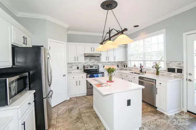 a kitchen that has a lot of white cabinets and stainless steel appliances