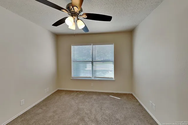 an empty room with a chandelier fan and windows