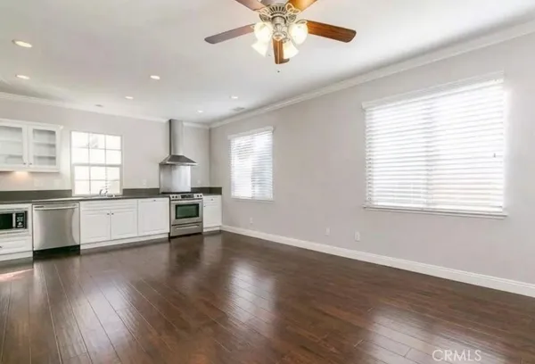 a view of an empty room with wooden floor and a kitchen