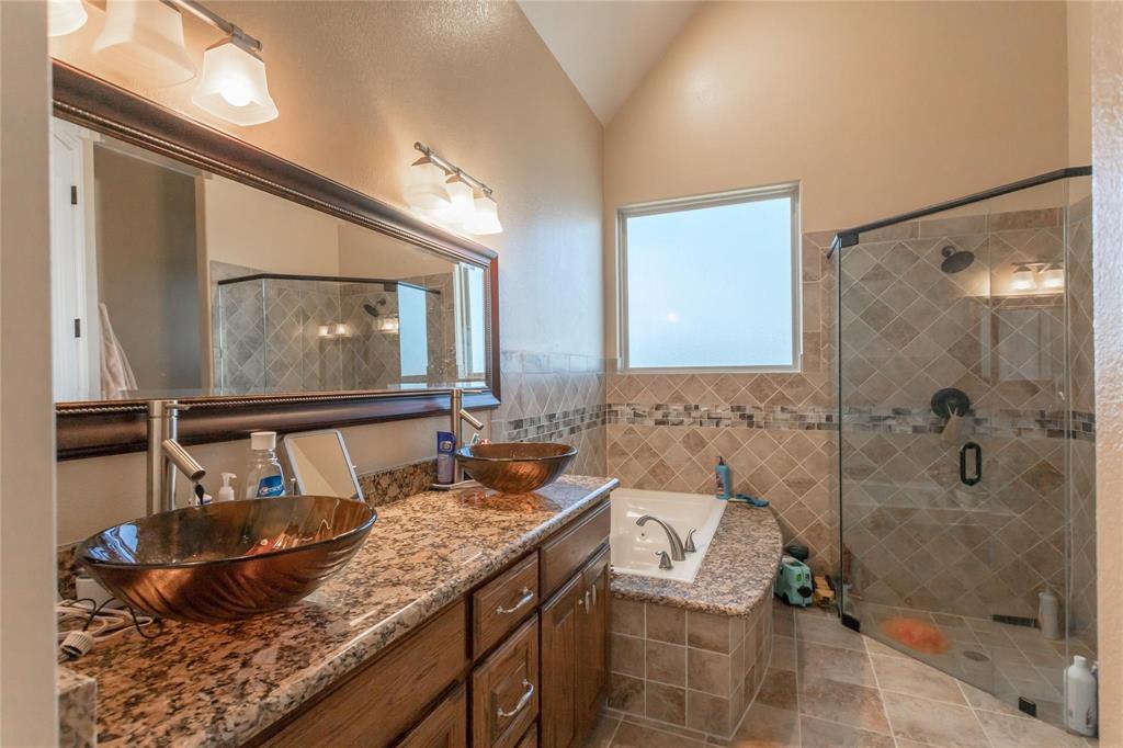8900 Holly Road Alvarado, TX 76009 - Photo 10 of 17 Dual vessel sinks with bronze-finish basins, granite-style countertops, wood-finish cabinetry, and a large soaking tub with tiled surround