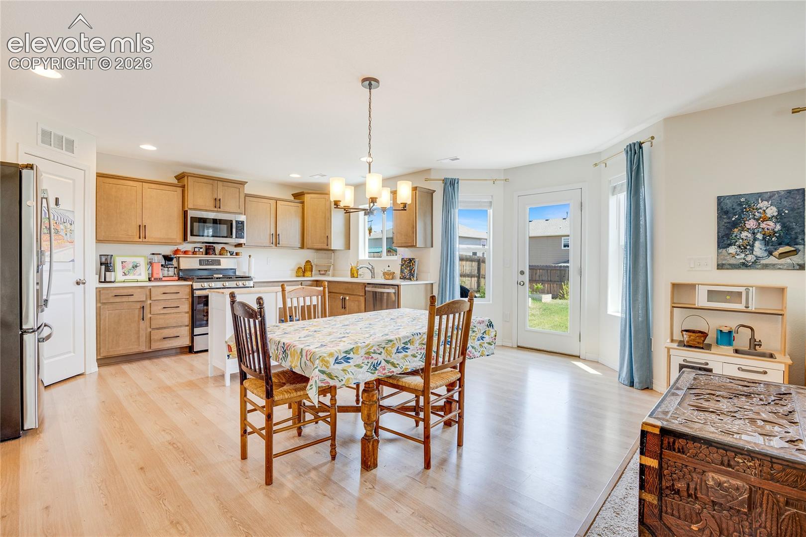 Open-concept kitchen and dining area featuring light wood-finish flooring, light wood cabinetry, white countertops, and stainless steel appliances