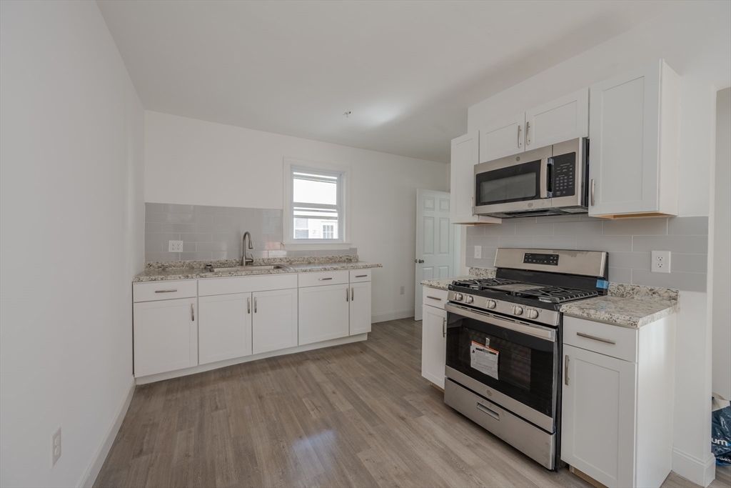 348 Walker Street Lowell, MA 01851 - Photo 19 of 20 a kitchen with granite countertop wooden floor stainless steel appliances a sink cabinets and a window