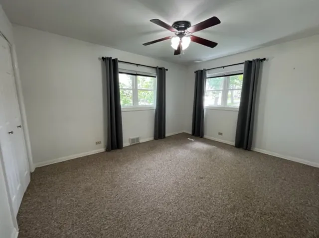an empty room with chandelier fan and windows