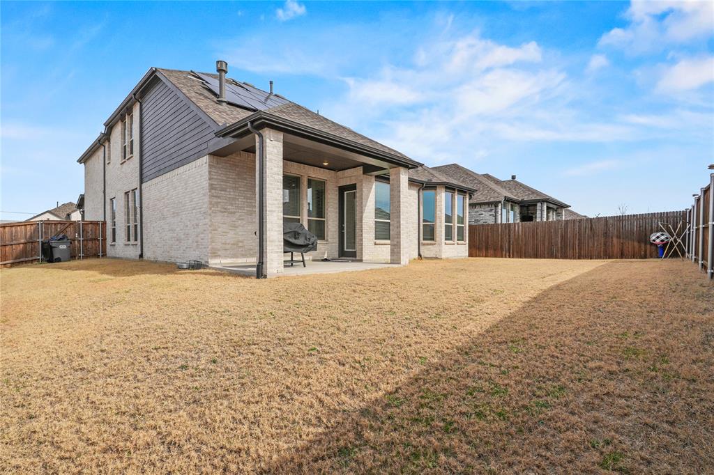 1805 Lockhart Drive Forney, TX 75126 - Photo 18 of 22 Back of house with roof mounted solar panels, brick siding, a fenced backyard, and a patio area