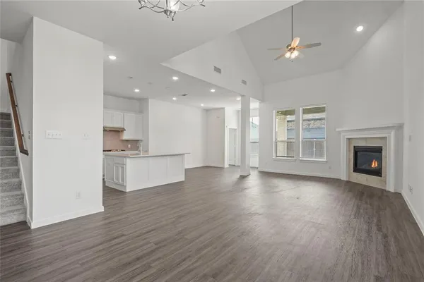 an empty room with wooden floor kitchen view and a fireplace