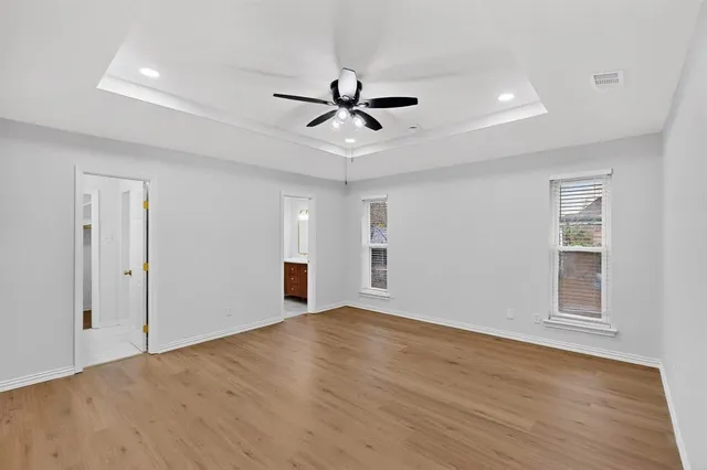 an empty room with wooden floor ceiling fan and windows