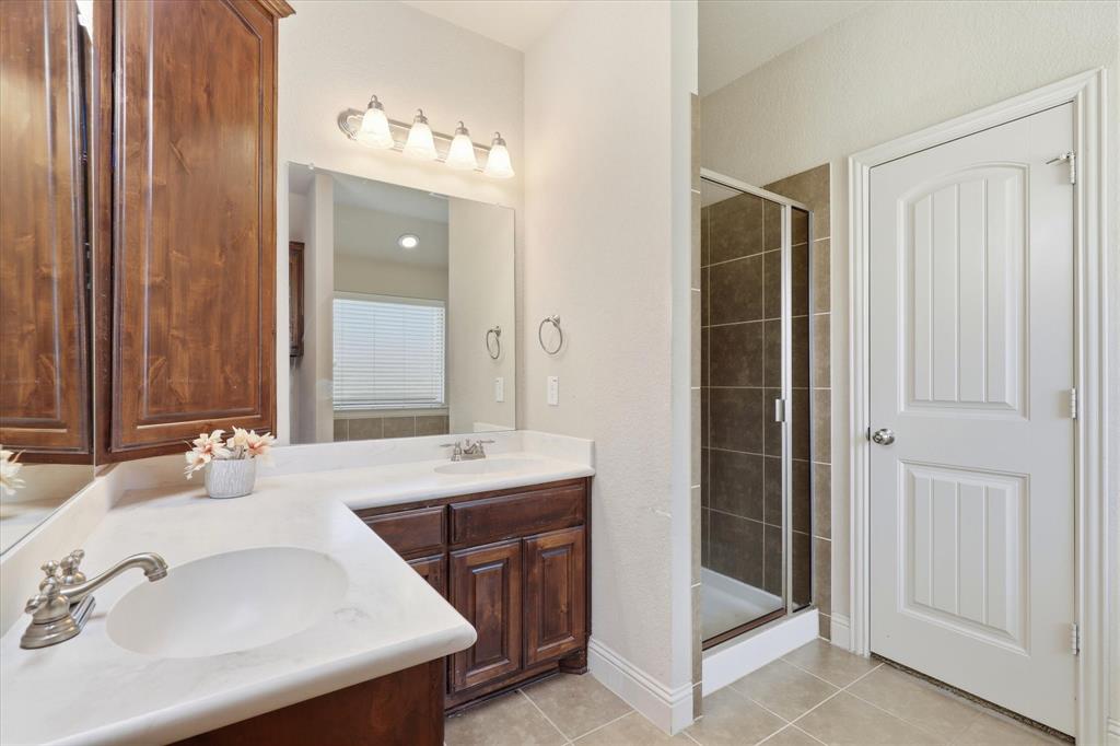 115 Blue Quail Road Red Oak, TX 75154 - Photo 16 of 35 Dual vanity with integrated sinks, wood-finish cabinetry, frameless glass shower enclosure, and tiled flooring